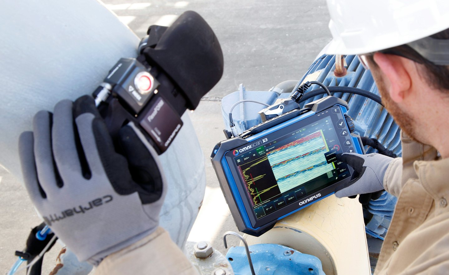 Técnico usa un sensor y una tableta para probar una tubería industrial.