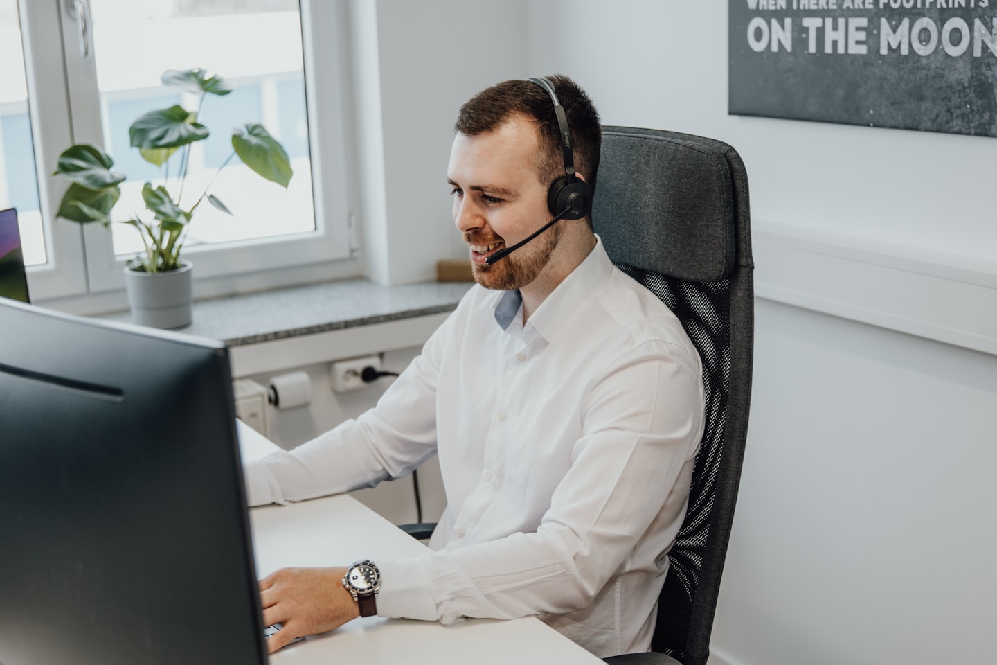 Hombre con auriculares sonríe mientras trabaja en una computadora.