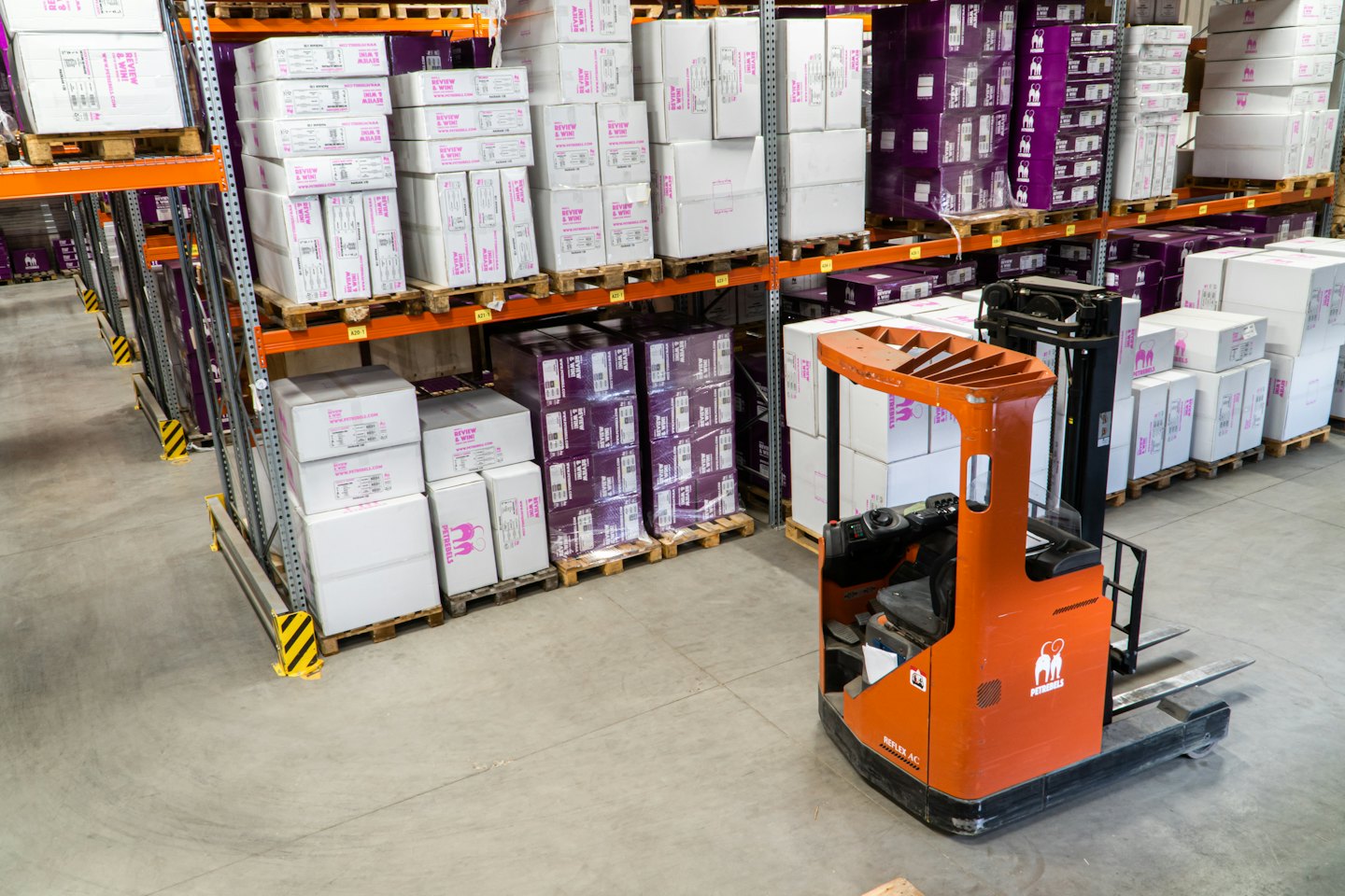 Carretilla elevadora naranja aparcada en un pasillo de almacén con cajas apiladas.