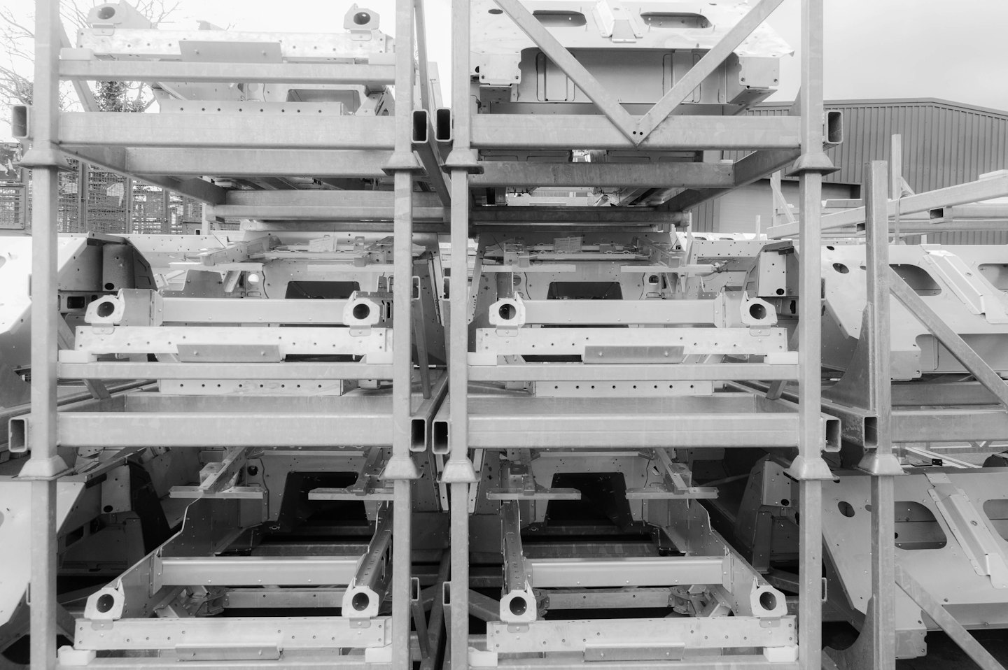 Chasis de coche de metal apilados en estanterías industriales al aire libre.